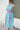 Mannequin wearing a holiday patterned apron with a pink belt against a white wall.