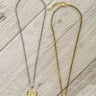 Two necklaces, one silver and one gold, on a wooden surface.