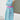 Mannequin wearing a holiday patterned apron with a pink belt against a white wall.