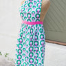 Mannequin wearing a holiday patterned apron with a pink belt against a white wall.
