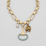 A gold-toned chunky chain necklace with multiple charms, including a small clear rhinestone, a horse-head charm, and a hammer-shaped charm outlined with turquoise stones, displayed on a beige fabric jewelry bust.
