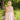 Woman in a light pink dress with bee patterns standing in a natural setting with greenery.