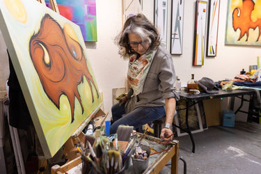 Artist working on a painting in an art studio with various artworks on the walls.